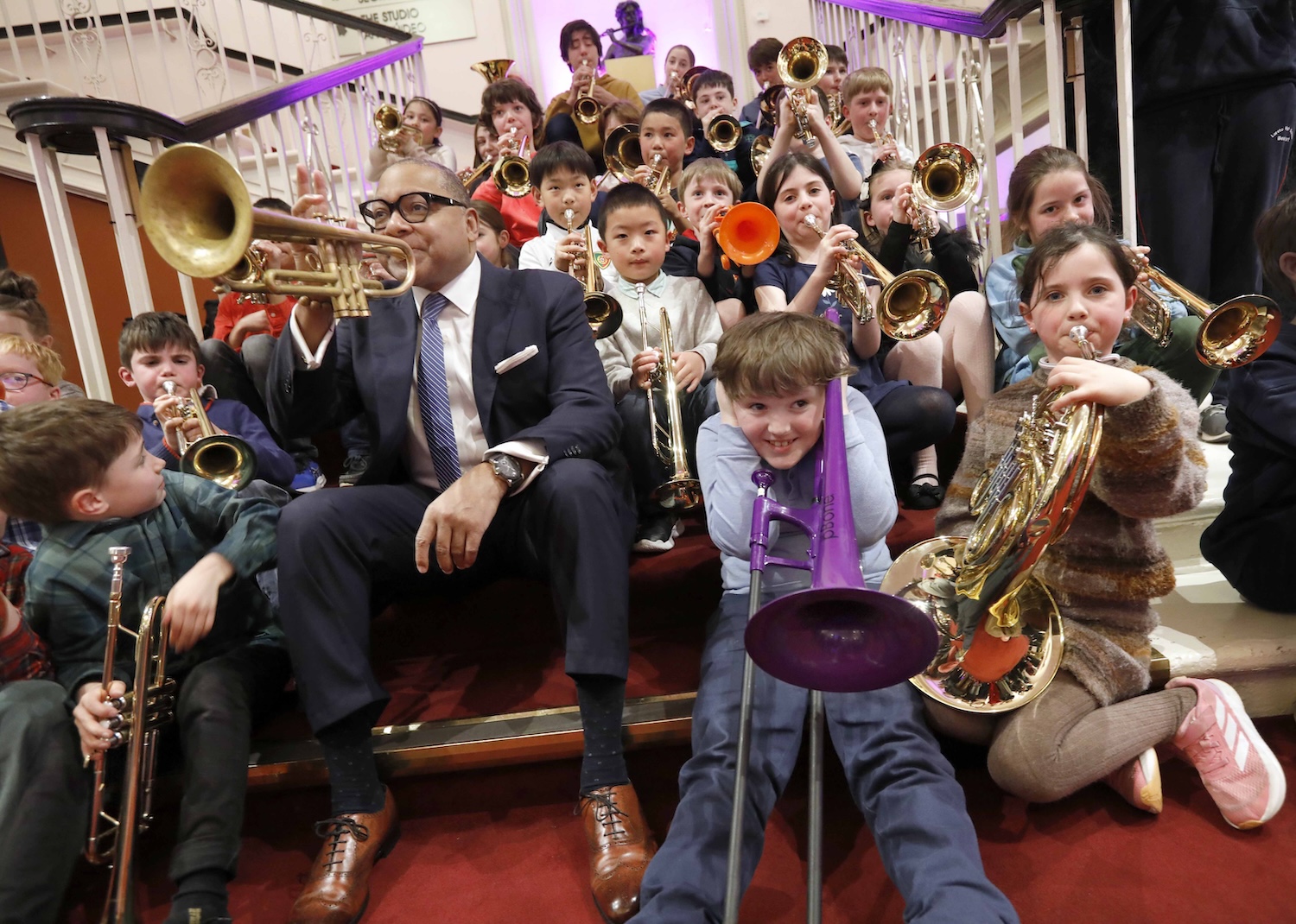 Wynton Marsalis plaing the trumpet with a group of children holding and playing brass instruments